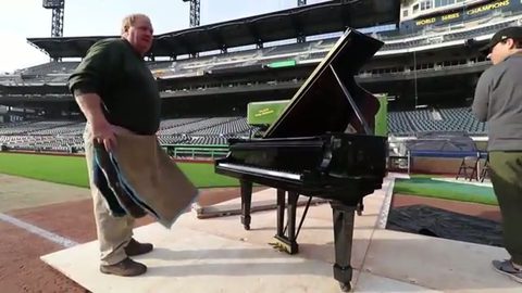 mover shaking out a moving blanket beside a grand piano on a board, face visible